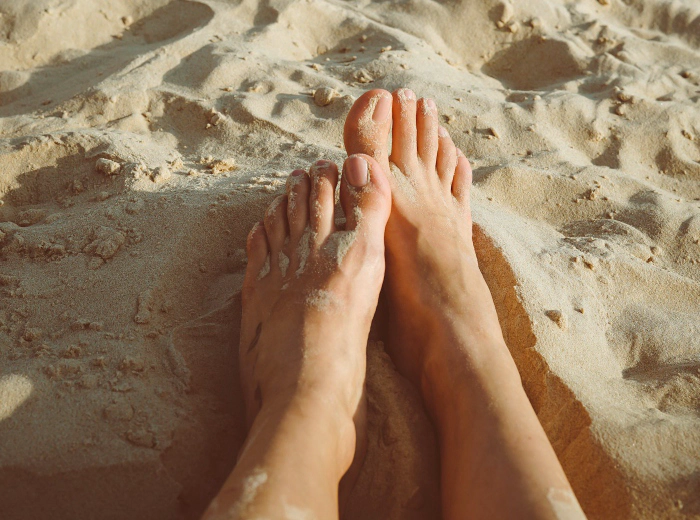 Bare feet resting on warm sand at the beach, healthy and relaxed