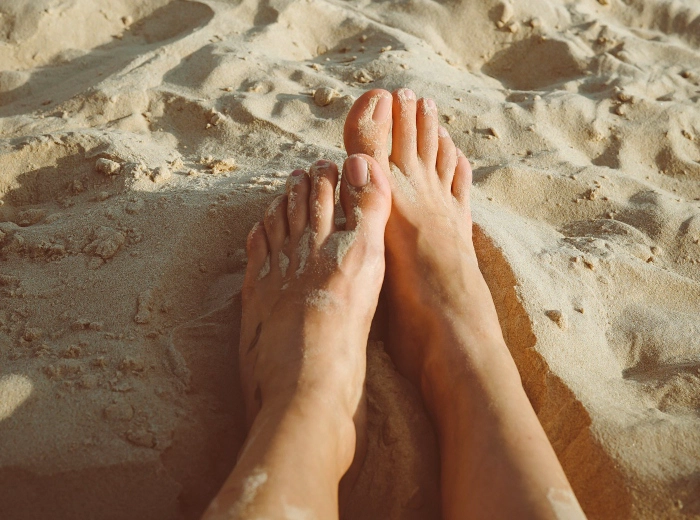 Bare feet resting on warm sand at the beach, healthy and relaxed